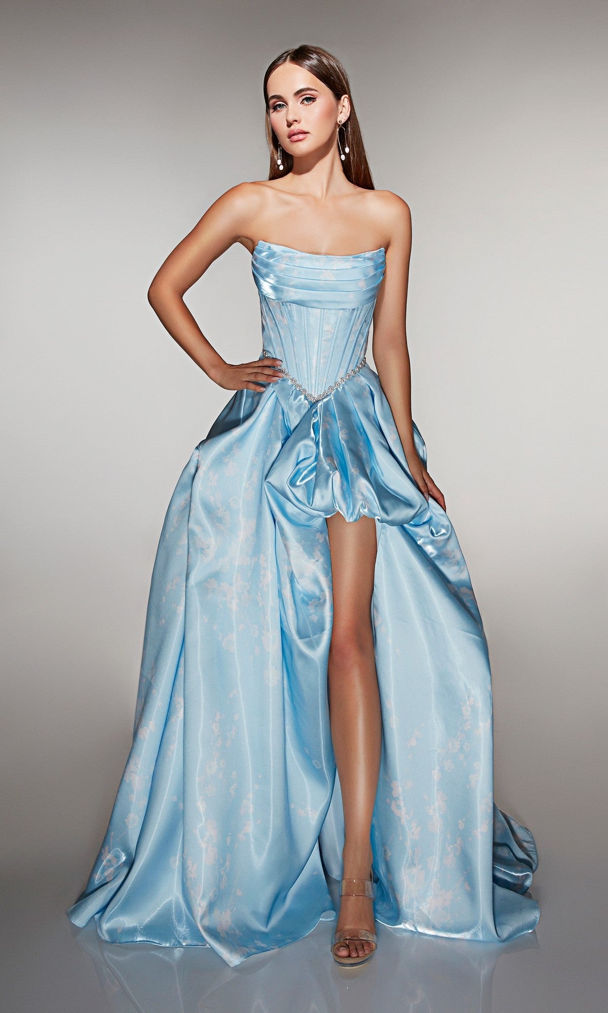 A woman poses against a plain light background wearing the Alyce 61989 long prom dress: a strapless satin ball gown in light blue with a corset bodice, high-leg slit, and voluminous skirt.